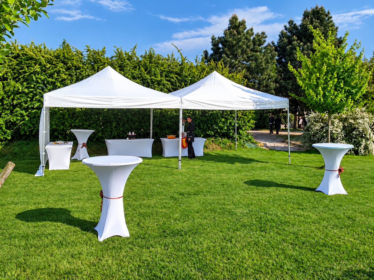 Jardin de la ferme : pelouse, tentes blanches et mange-debout dressés pour une réception