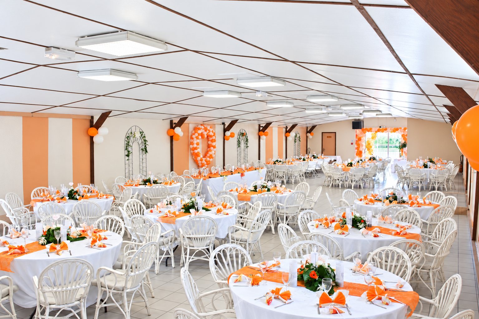 Grande salle de réception aux tables rondes et chaises en rotin blanc, décor orange